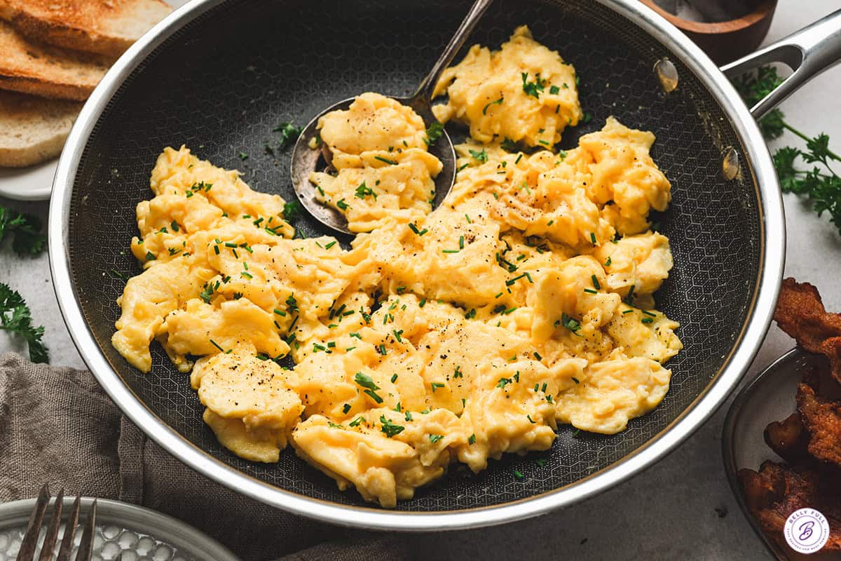 Soft fluffy scrambled eggs in a skillet with fresh herbs and cracked black pepper.