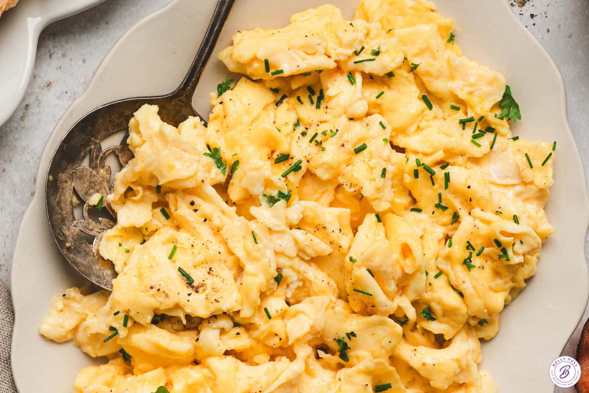 Close-up of creamy scrambled eggs with soft curds garnished with fresh chives and parsley.