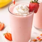Side view of a glass of strawberry banana orange julius in a glass with whipped cream and a strawberry.