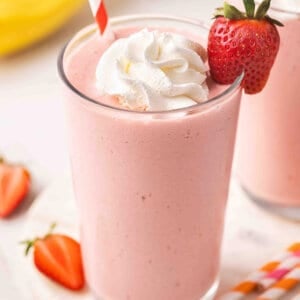 Side view of a glass of strawberry banana orange julius in a glass with whipped cream and a strawberry.