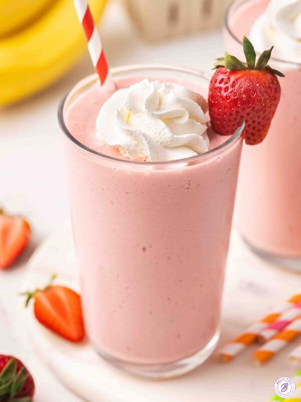 Side view of a glass of strawberry banana orange julius in a glass with whipped cream and a strawberry.