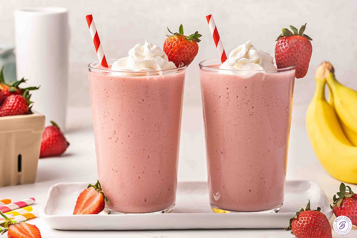 Two strawberry banana orange Julius drinks topped with whipped cream and a strawberry.
