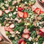Strawberry spinach salad with fresh strawberries, mushrooms, avocado, goat cheese, sliced almonds, and scallions tossed in creamy poppy seed dressing on a serving platter.