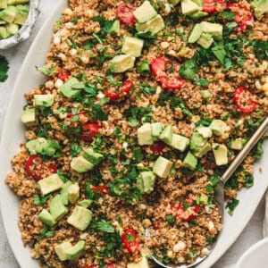 Toasted quinoa salad with avocado, cherry tomatoes, corn, scallions, and cilantro on a large serving platter.