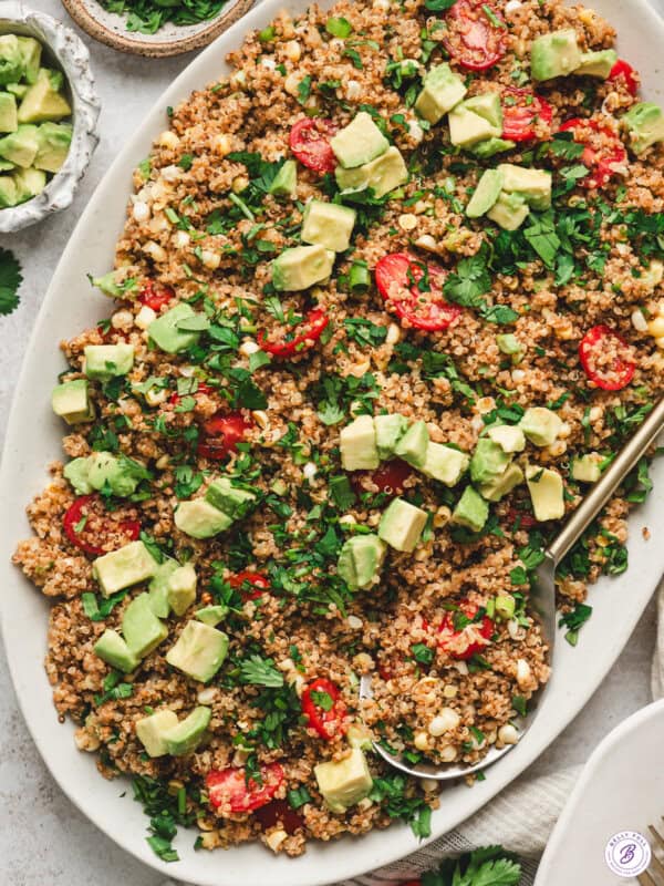 Toasted quinoa salad with avocado, cherry tomatoes, corn, scallions, and cilantro on a large serving platter.