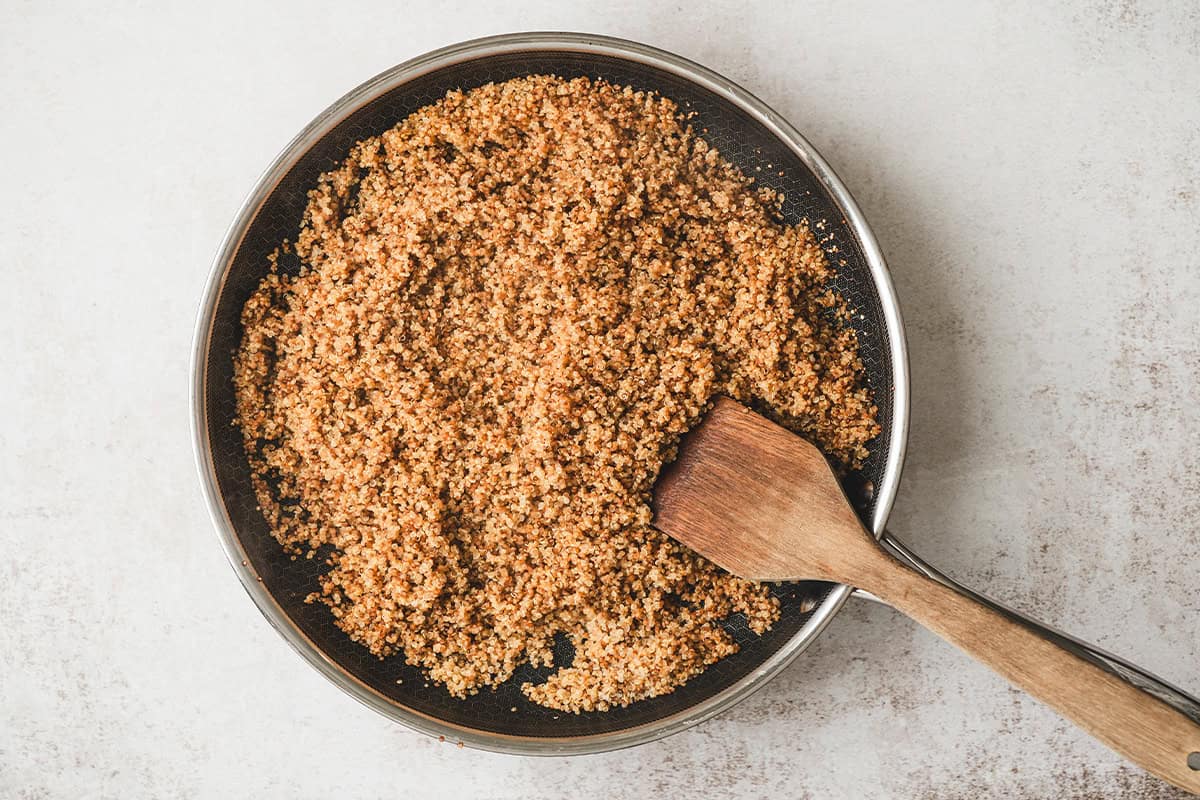 Cooked toasted quinoa in a skillet after absorbing the water and turning fluffy.
