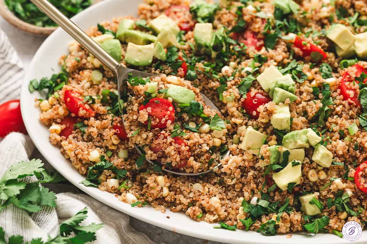 Spoon scooping toasted quinoa salad with avocado, corn, tomatoes, and fresh cilantro.