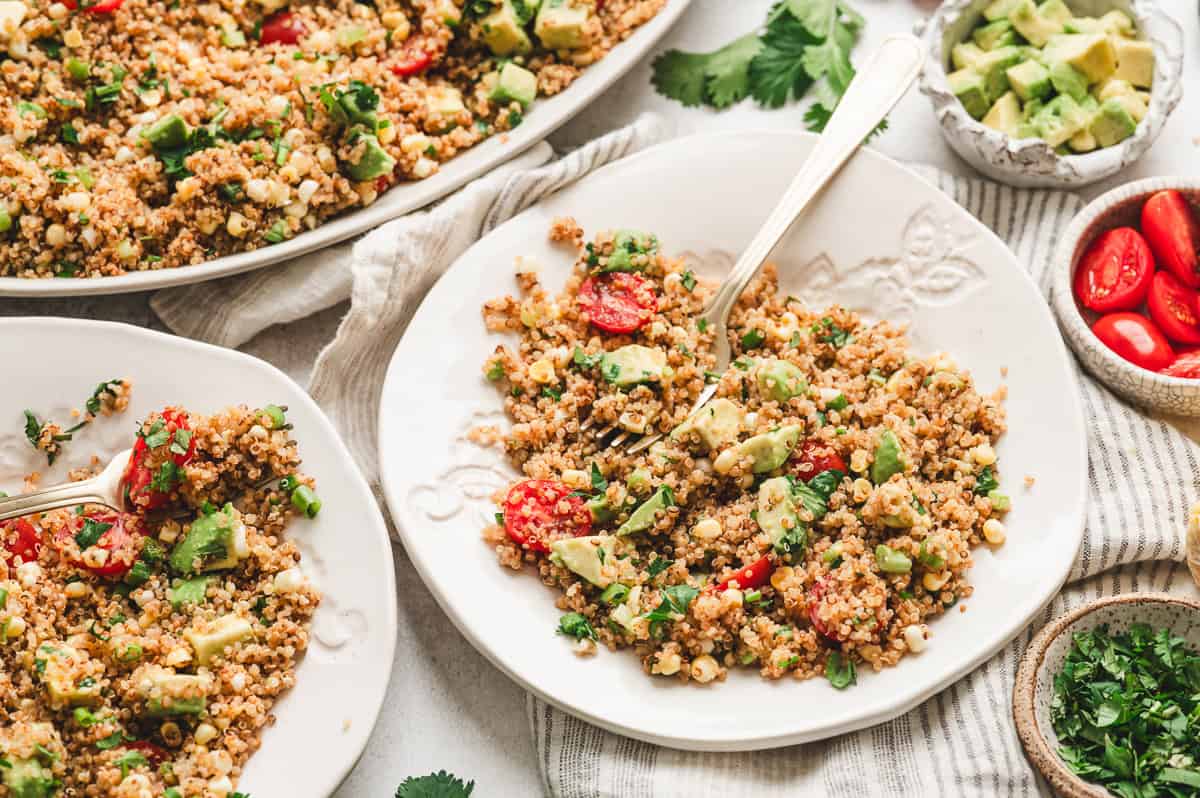 Bowls of toasted quinoa salad topped with avocado, cherry tomatoes, corn, scallions, and cilantro.