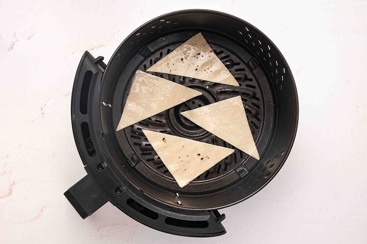 Wonton wrapper halves in an air fryer basket.