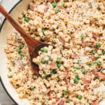 Creamy bacon pea pasta in a skillet topped with grated Parmesan cheese and served with a wooden spoon.