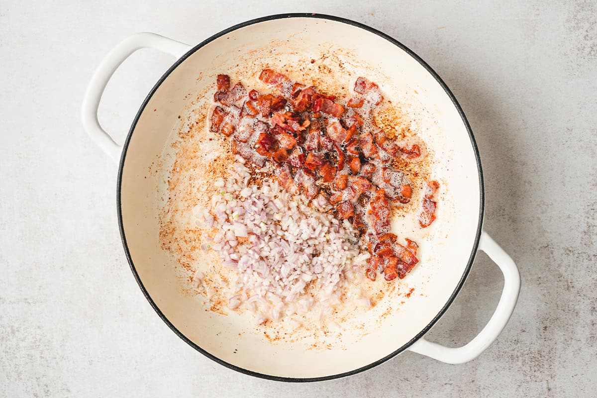 Crispy bacon and minced shallots cooking in a large skillet.