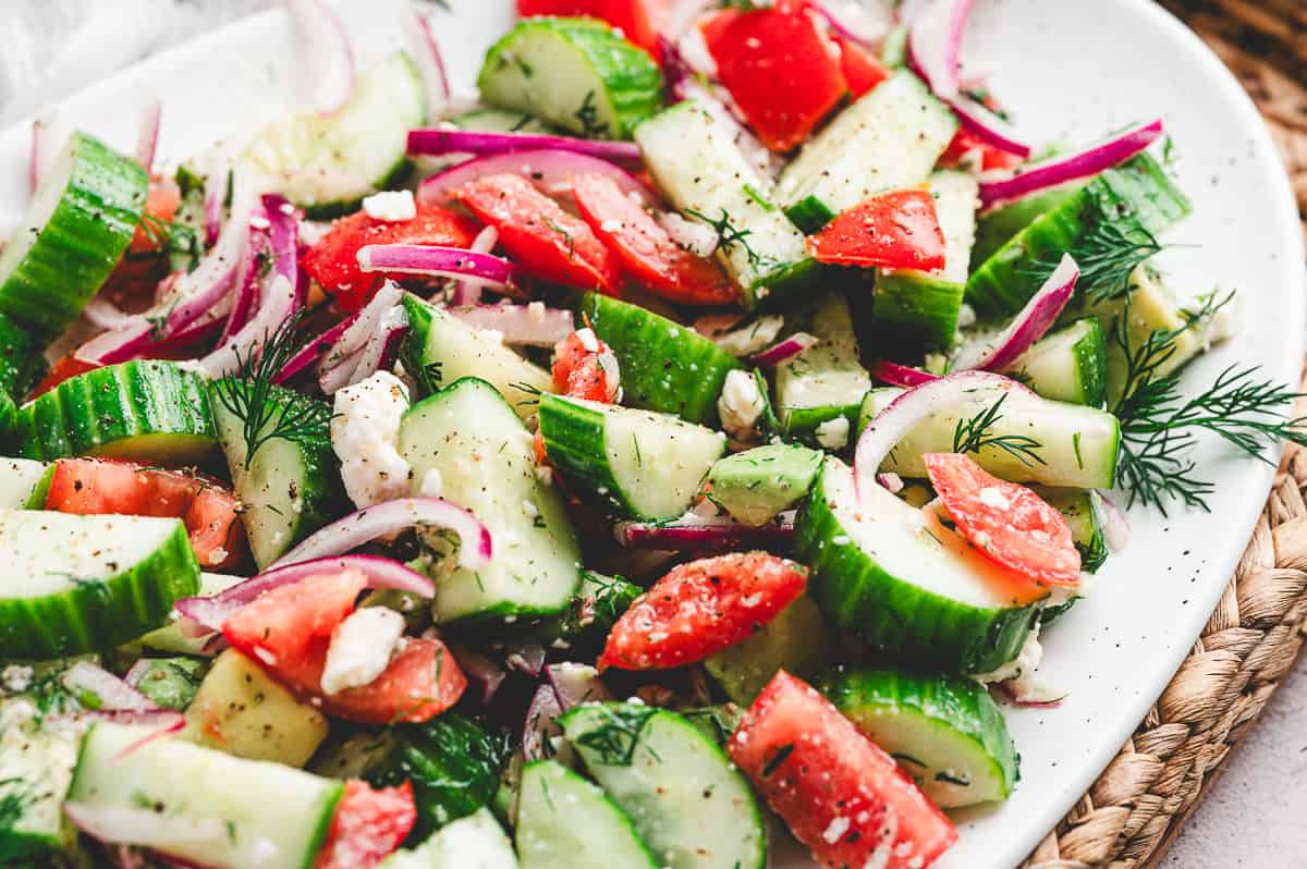 Close up of cucumber tomato salad with red onion, crumbled feta, and fresh dill on a white serving platter