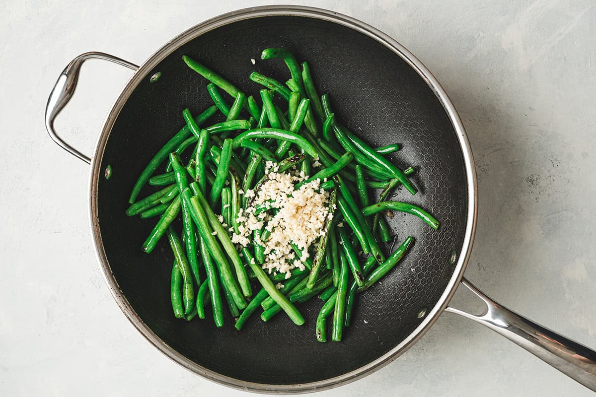 Minced garlic added to a skillet with green beans.