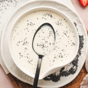 Creamy homemade poppy seed dressing in a white serving bowl with a black spoon and scattered poppy seeds.