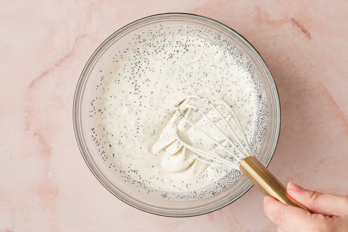 Whisk stirring creamy poppy seed dressing in a glass mixing bowl during preparation.
