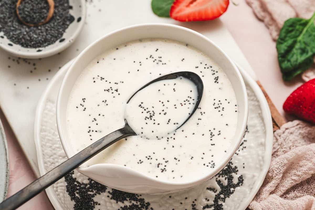 Homemade poppy seed dressing in a white bowl garnished with poppy seeds and fresh strawberries.