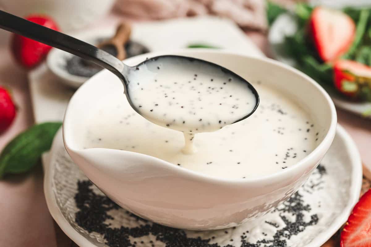 Spoon lifting creamy poppy seed dressing from a serving bowl, showing its smooth, pourable consistency.
