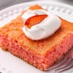 Side view of a slice of soda cake on a plate, topped with Cool whip and a strawberry.