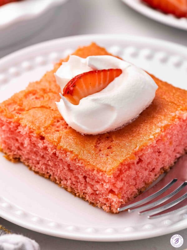 Side view of a slice of soda cake on a plate, topped with Cool whip and a strawberry.