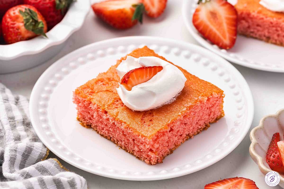 A slice of strawberry soda cake on a plate topped with Cool whip and a strawberry.