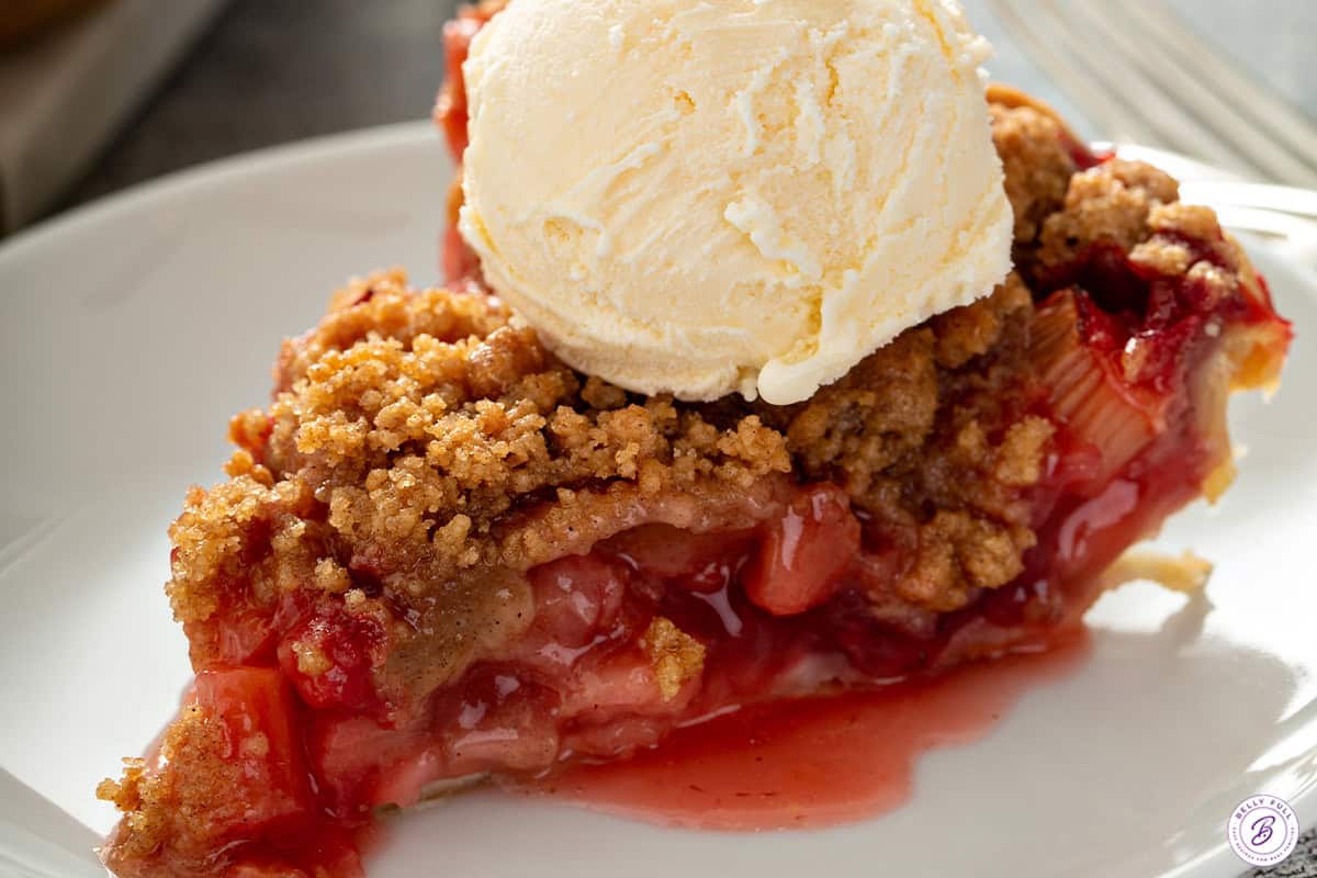 Close-up of a slice of strawberry rhubarb pie with crumb topping and melting vanilla ice cream.
