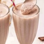 Two tall glasses of homemade Wendy's Frosty copycat with a gold spoon scooping the thick, creamy chocolate mixture