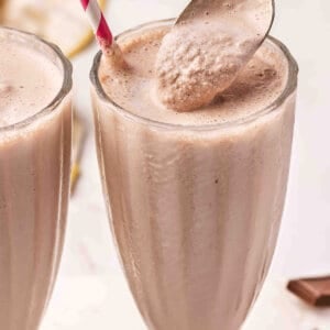 Two tall glasses of homemade Wendy's Frosty copycat with a gold spoon scooping the thick, creamy chocolate mixture