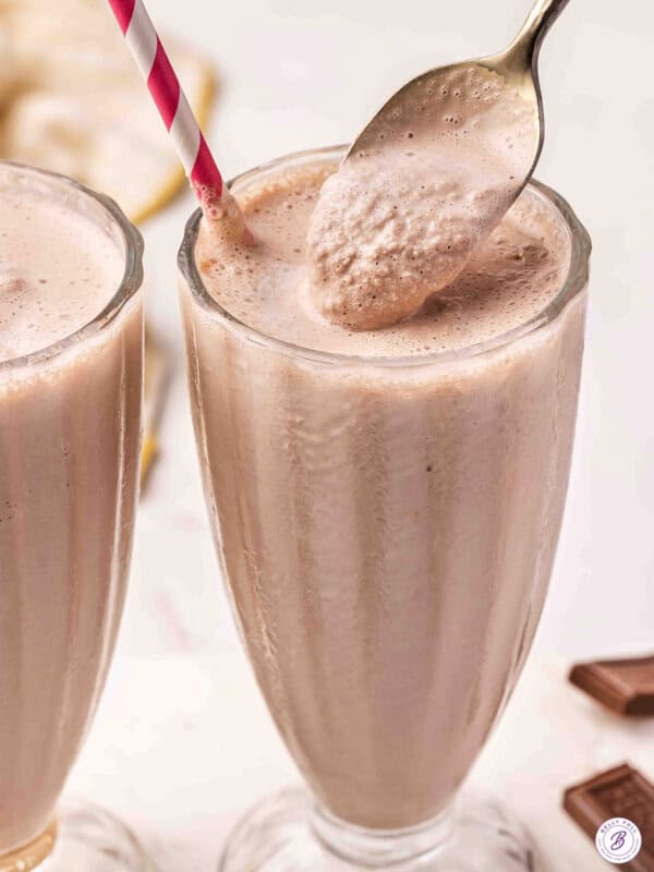 Two tall glasses of homemade Wendy's Frosty copycat with a gold spoon scooping the thick, creamy chocolate mixture