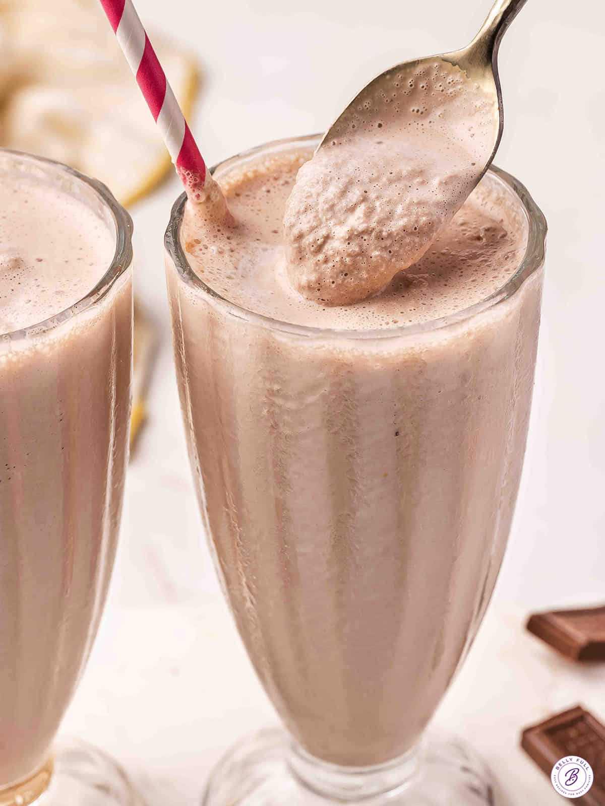 Two tall glasses of homemade Wendy's Frosty copycat with a gold spoon scooping the thick, creamy chocolate mixture