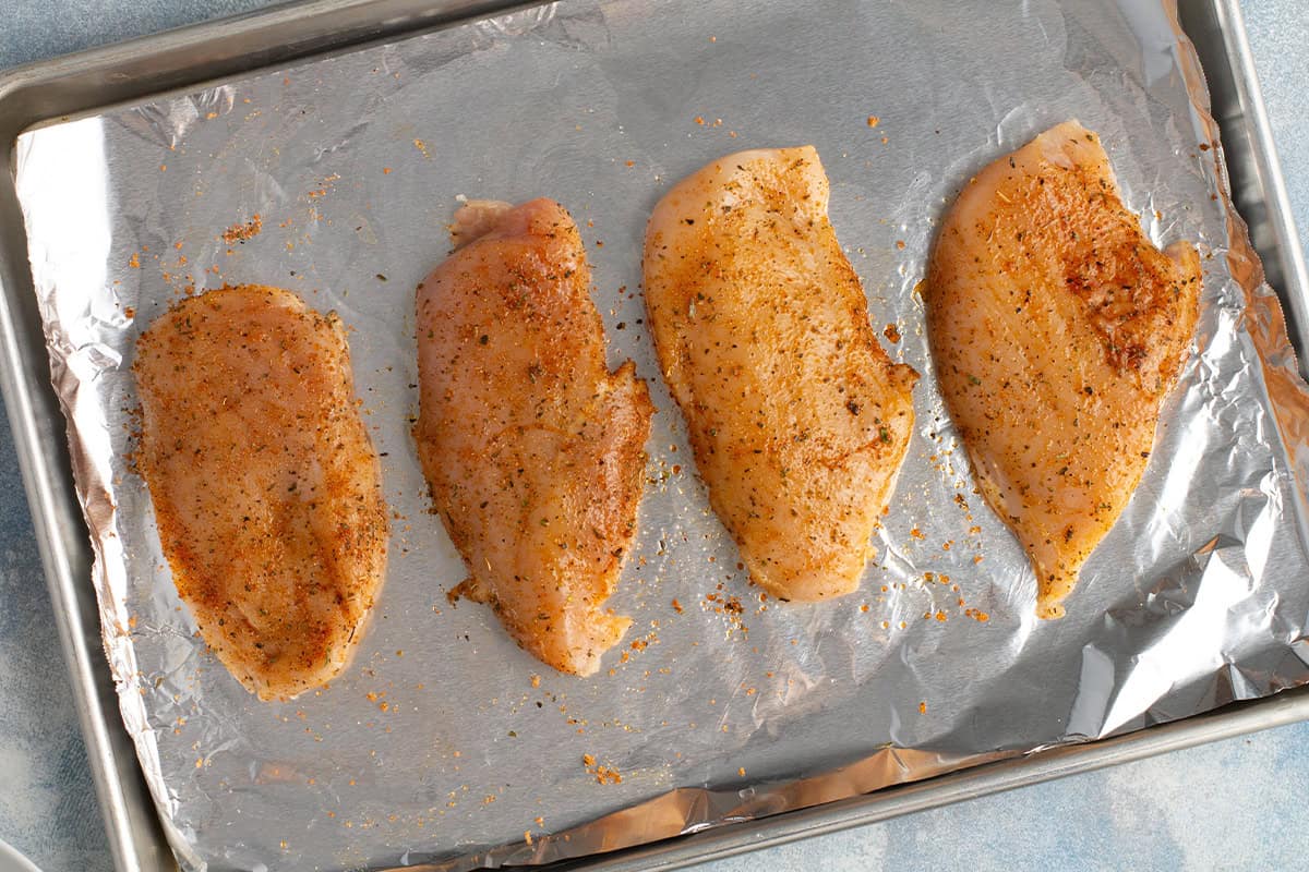 seasoned chicken breasts on a foil lined baking sheet ready to bake