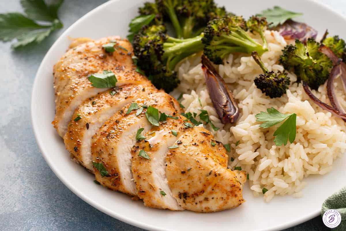 sliced baked chicken breast on a plate with rice pilaf and roasted broccoli