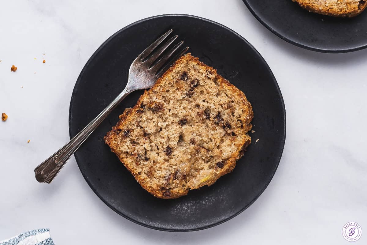 sliced banana bread on a platter with fresh bananas, chocolate chips, walnuts, and butter
