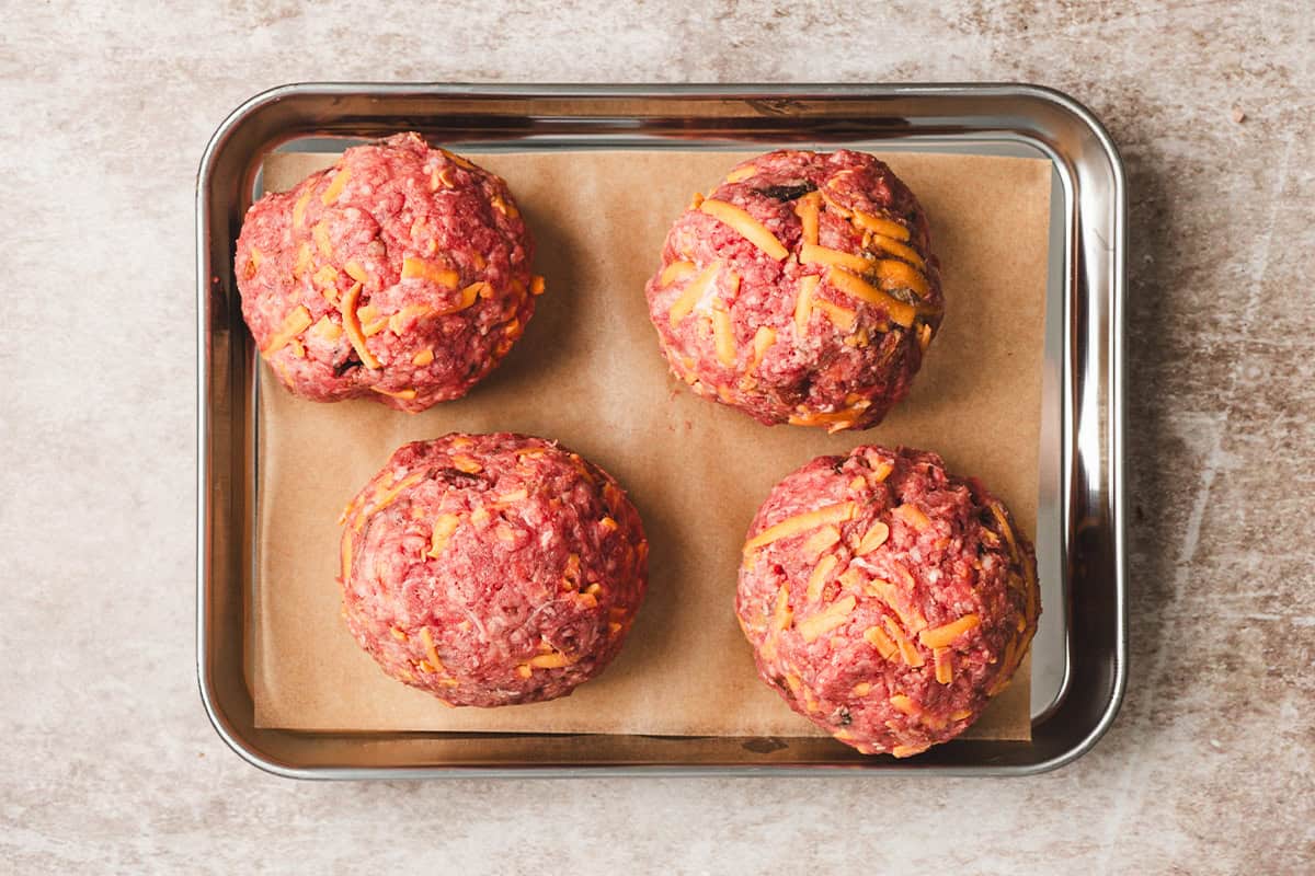 Four meatballs for crack smash burgers on a baking sheet.