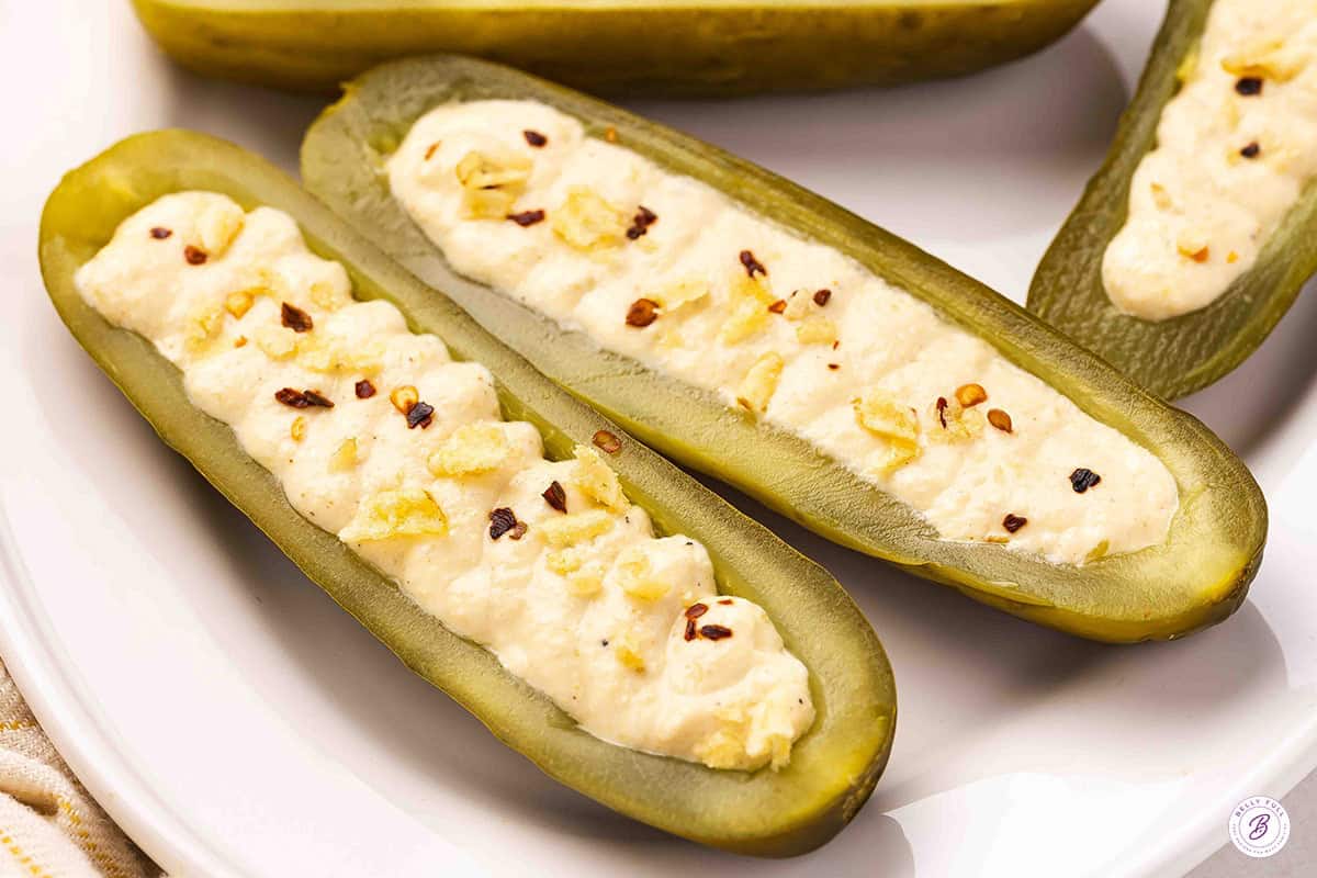 Deviled pickles on a plate topped with red pepper flakes and crushed potato chips.