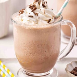 Frozen hot chocolate in a glass mug topped with whipped cream and chocolate shavings, with a striped straw