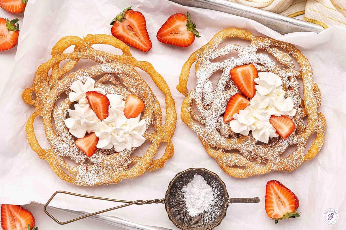Two funnel cakes topped with whipped cream and strawberries.
