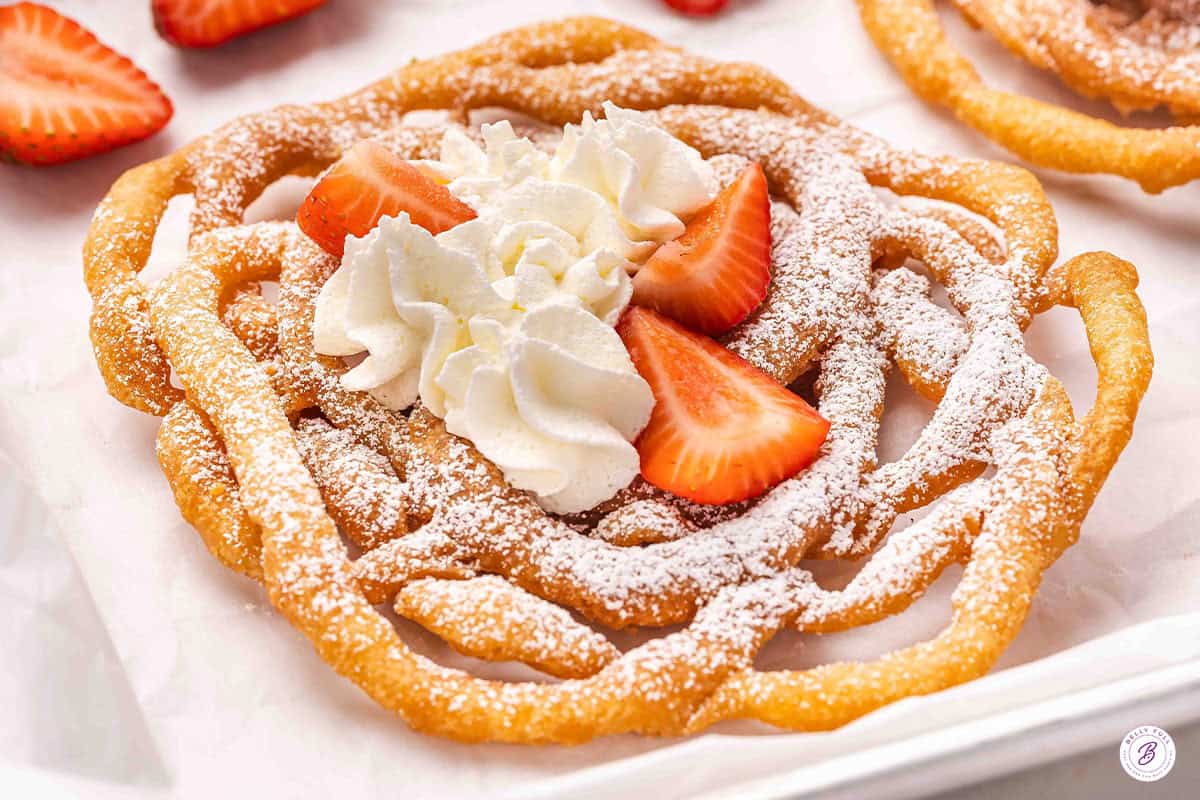 A homemade funnel cake topped with whipped cream and strawberries.