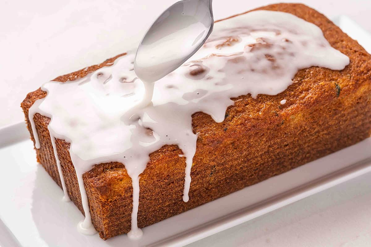 Lemon glaze being drizzled on a lemon zucchini loaf.