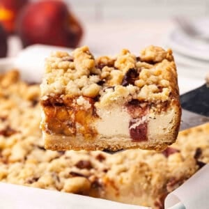 Side view of a peach cobbler cheesecake bar being lifted out of a baking dish.