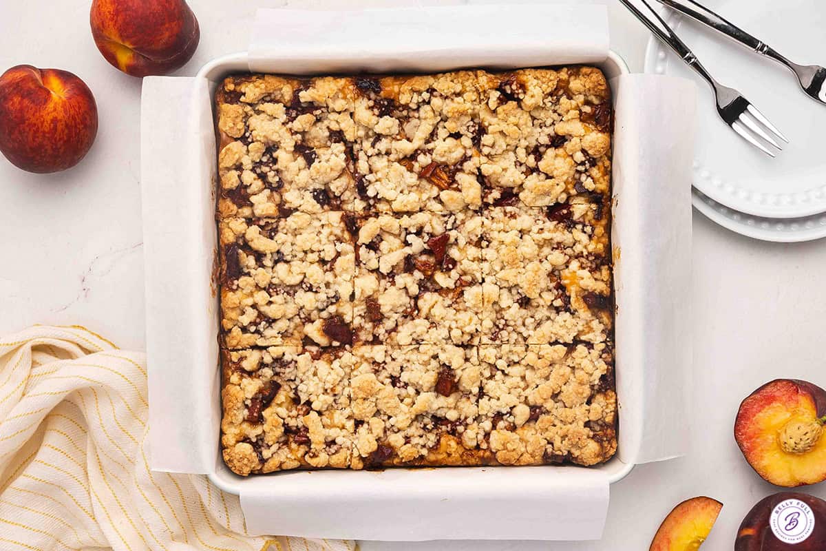 Overhead view of a baking dish of peach cobbler cheesecake bars before slicing.