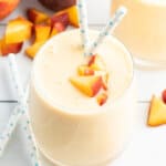peach smoothie in glass with peach cubes and straw