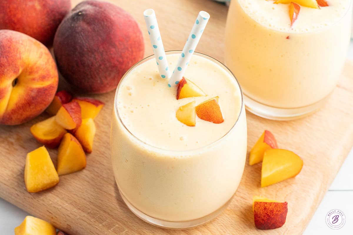 peach smoothie in glass with peach cubes and straw