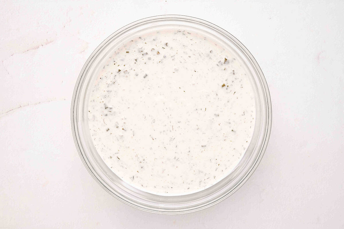 Overhead view of finished homemade ranch dressing in a glass bowl, smooth and speckled with herbs