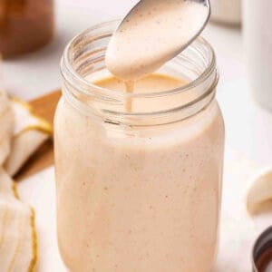 Yum Yum Sauce drizzling off a spoon into a mason jar, showing its smooth, pourable consistency