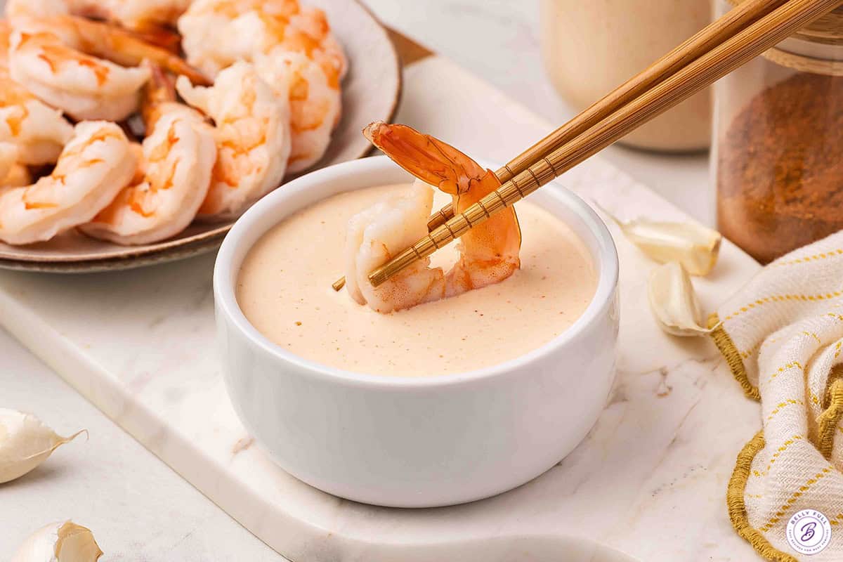 Shrimp being dipped into a bowl of creamy Yum Yum Sauce with chopsticks