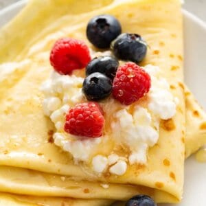 Folded blini topped with cottage cheese, raspberries, and blueberries, drizzled with honey