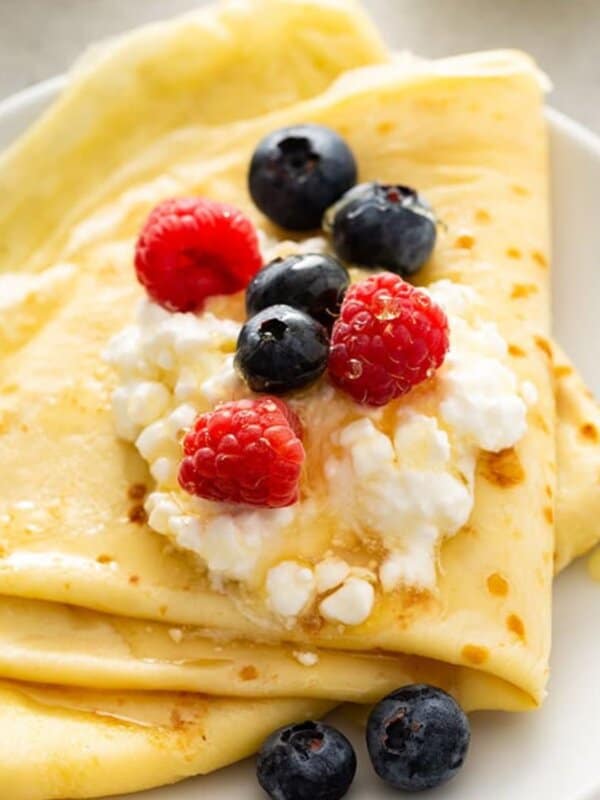 Folded blini topped with cottage cheese, raspberries, and blueberries, drizzled with honey