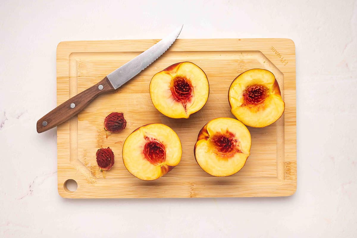 Peaches sliced in half on a cutting board with the pits removed.