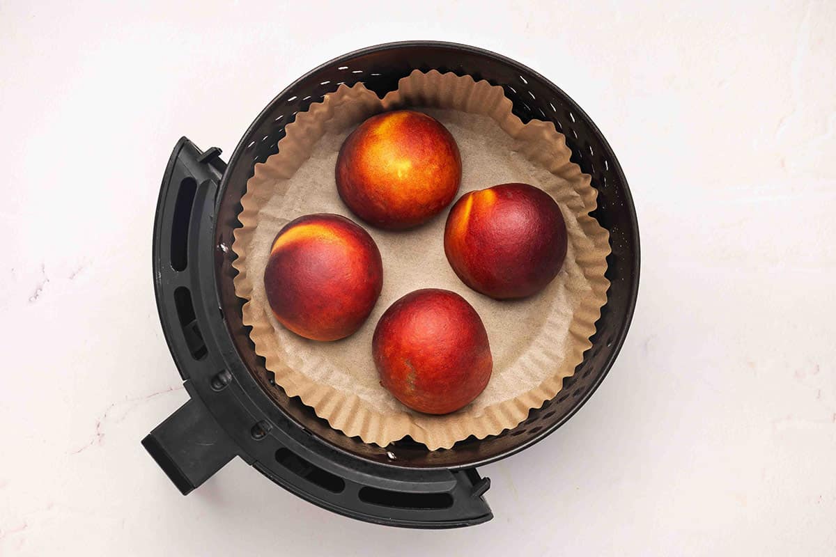 Peach halves in an air fryer basket.