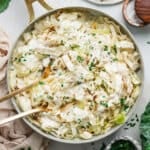 Overhead view of a skillet with alfredo cabbage ribbons with kitchen tongs.